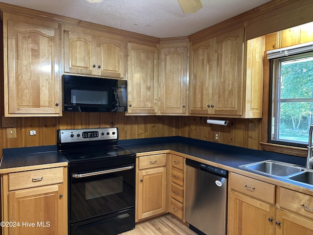 kitchen with light wood-type flooring, sink, black appliances, and wooden walls