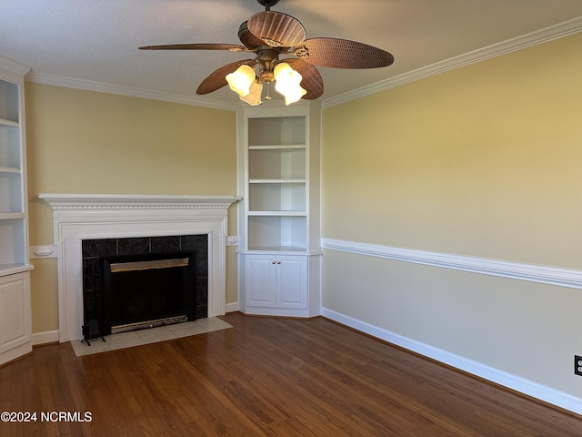 unfurnished living room featuring built in shelves, a tile fireplace, ornamental molding, ceiling fan, and hardwood / wood-style floors