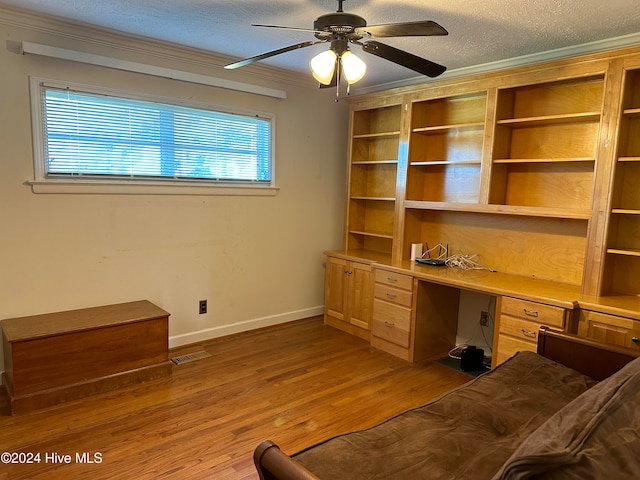 unfurnished office featuring ceiling fan, crown molding, a textured ceiling, built in desk, and hardwood / wood-style flooring