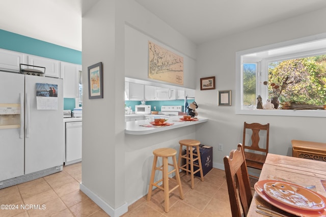 kitchen with white cabinets, a kitchen breakfast bar, white appliances, and light tile patterned flooring