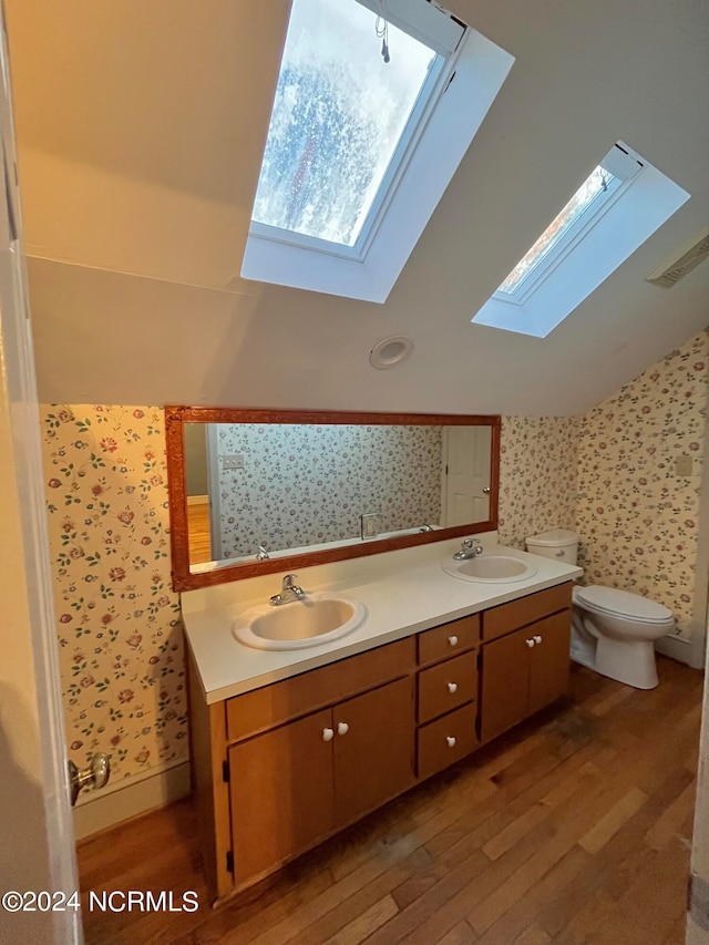 bathroom with vanity, lofted ceiling with skylight, toilet, and wood-type flooring