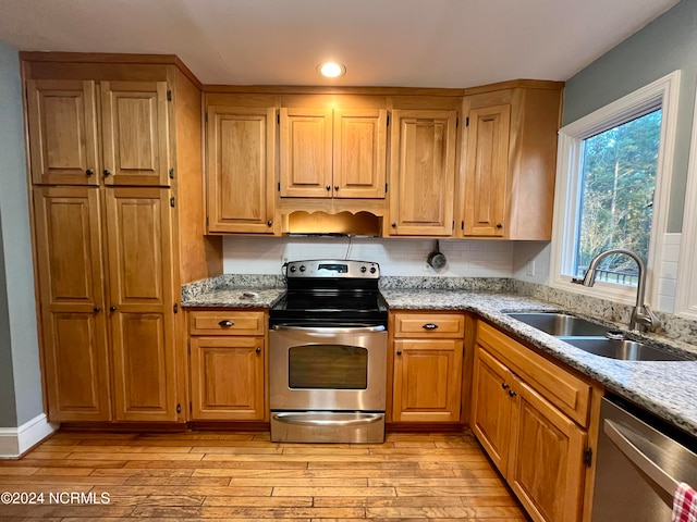 kitchen with appliances with stainless steel finishes, sink, light wood-type flooring, light stone counters, and decorative backsplash