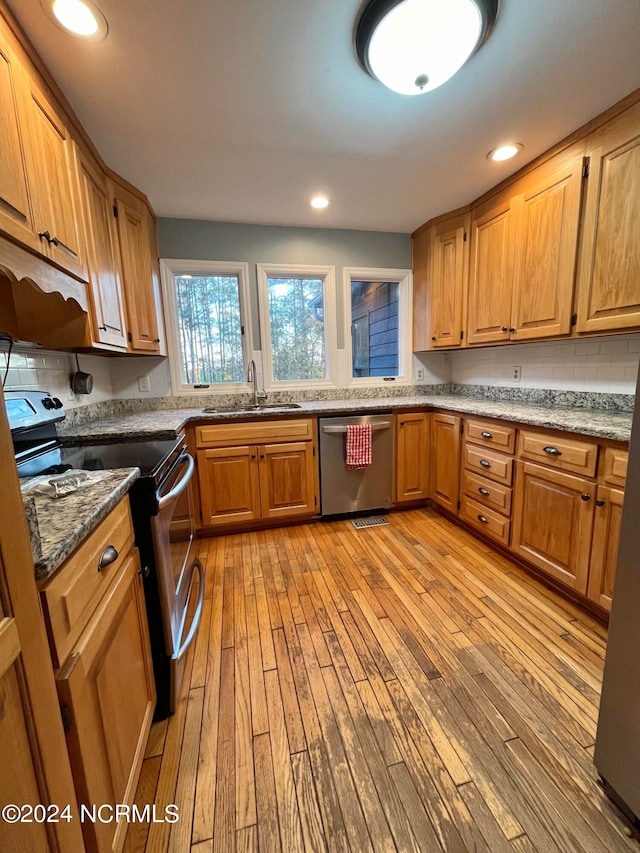 kitchen featuring dark stone countertops, stainless steel appliances, sink, and light wood-type flooring