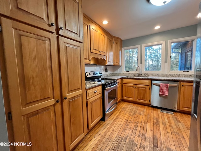 kitchen with light stone counters, sink, appliances with stainless steel finishes, and light hardwood / wood-style flooring