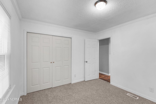 unfurnished bedroom with a textured ceiling, carpet floors, a closet, and crown molding