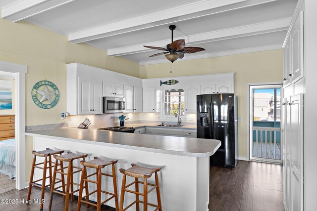 kitchen featuring a peninsula, a sink, black fridge, a wealth of natural light, and stainless steel microwave