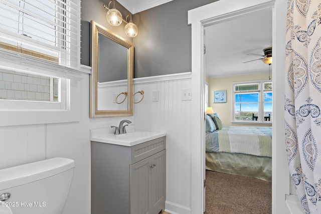 ensuite bathroom with toilet, ensuite bathroom, wainscoting, ceiling fan, and vanity