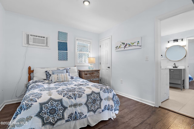 bedroom with a wall unit AC, a sink, baseboards, and wood finished floors