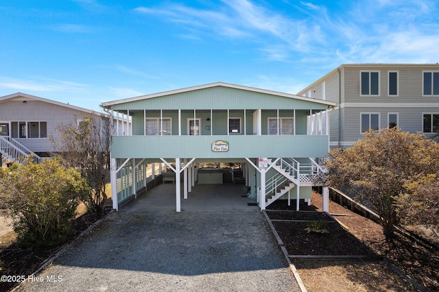 coastal inspired home featuring a carport, a sunroom, driveway, and stairs