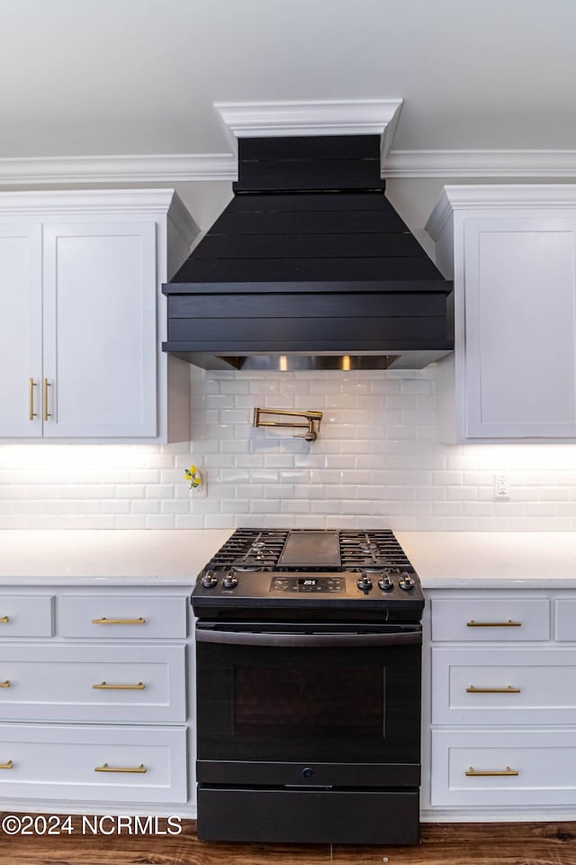 kitchen with decorative backsplash, stainless steel gas range oven, white cabinets, and premium range hood