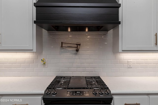 kitchen featuring black range with gas cooktop, light stone counters, decorative backsplash, and white cabinets