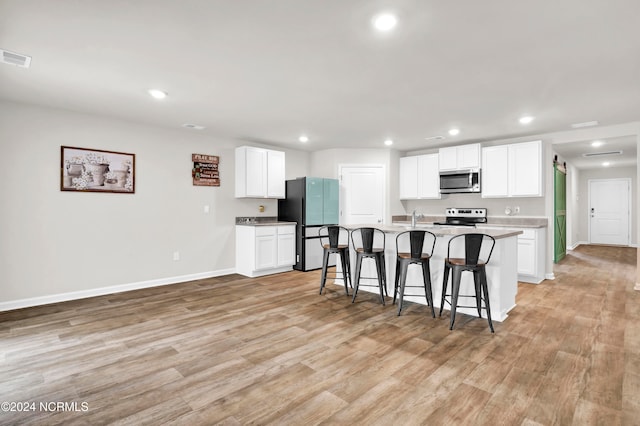 kitchen featuring light hardwood / wood-style flooring, a breakfast bar, white cabinetry, stainless steel appliances, and an island with sink