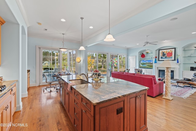 kitchen featuring sink, built in features, stone counters, a kitchen island with sink, and decorative light fixtures