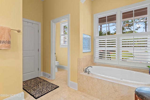 bathroom featuring tile patterned floors, a healthy amount of sunlight, toilet, and tiled tub