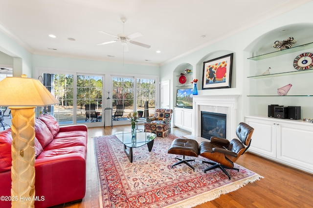 living room featuring ceiling fan, ornamental molding, light hardwood / wood-style floors, and built in features