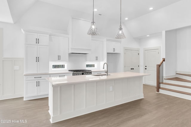 kitchen featuring light countertops, a sink, a center island with sink, range, and white cabinetry