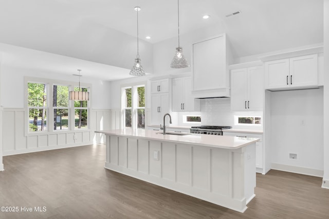 kitchen with vaulted ceiling, range, a center island with sink, light countertops, and premium range hood
