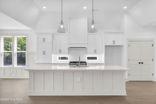 kitchen featuring white cabinets, light countertops, light wood finished floors, and a center island with sink
