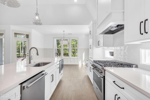 kitchen with a sink, custom range hood, light countertops, decorative light fixtures, and appliances with stainless steel finishes