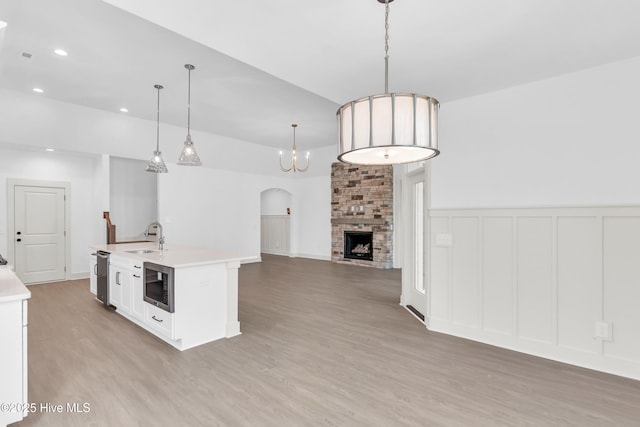 kitchen with light countertops, a sink, stainless steel microwave, light wood-style flooring, and open floor plan