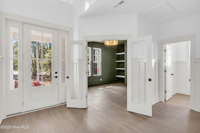 entrance foyer with wainscoting, a decorative wall, wood finished floors, and visible vents
