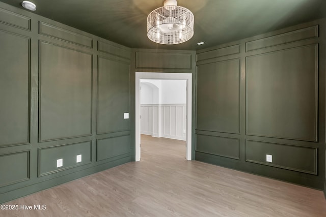 empty room with light wood-style flooring, a decorative wall, and an inviting chandelier