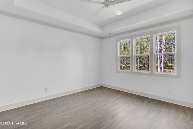 empty room featuring a tray ceiling, wood finished floors, a ceiling fan, and baseboards