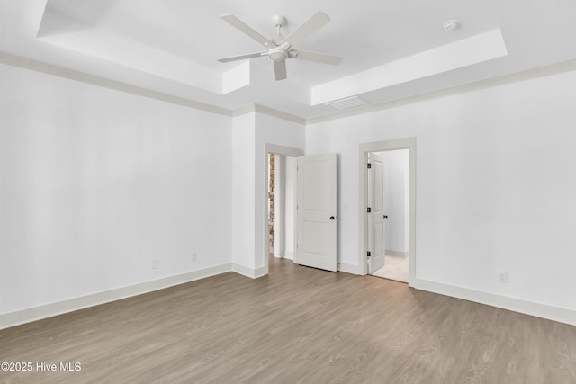 unfurnished bedroom featuring a raised ceiling, wood finished floors, and baseboards