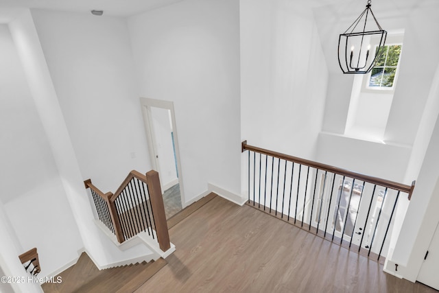 staircase with wood finished floors, a towering ceiling, and a chandelier
