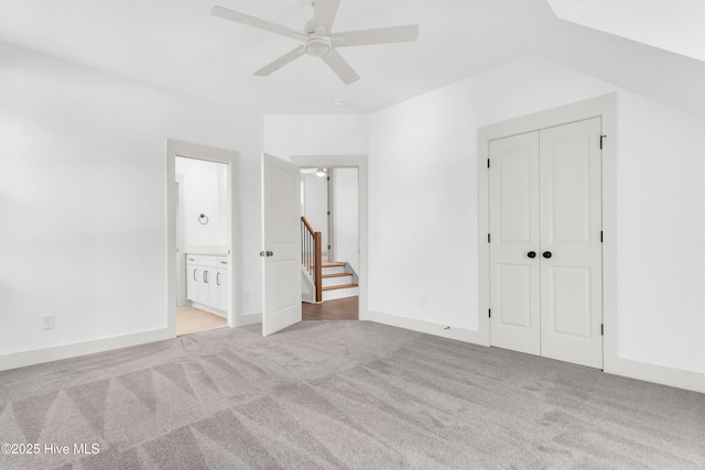 unfurnished bedroom featuring light colored carpet, ensuite bath, a ceiling fan, and a closet