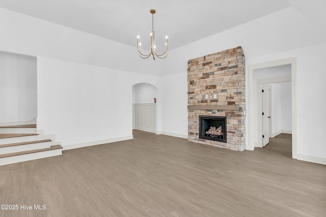 unfurnished living room with a fireplace, wood finished floors, arched walkways, and a notable chandelier