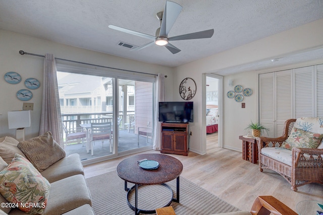 living room with ceiling fan, a textured ceiling, and light hardwood / wood-style flooring