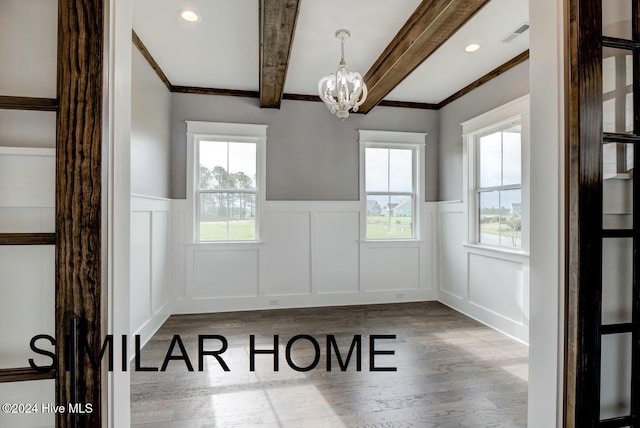 unfurnished dining area featuring a wealth of natural light, a notable chandelier, beamed ceiling, and wood finished floors