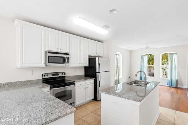 kitchen with appliances with stainless steel finishes, sink, white cabinets, light stone counters, and a kitchen island with sink