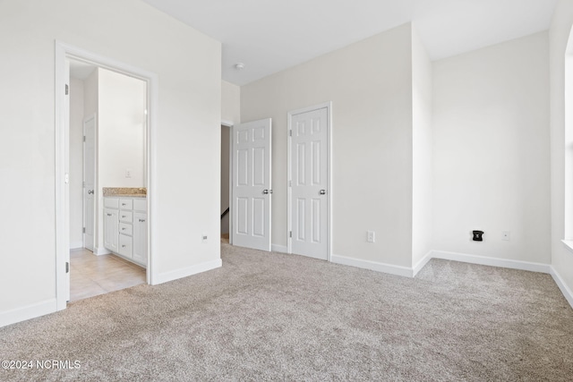 unfurnished bedroom with ensuite bathroom and light colored carpet