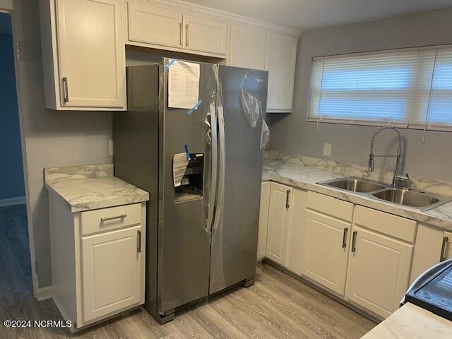 kitchen with stainless steel fridge, white cabinets, light wood-type flooring, sink, and light stone counters