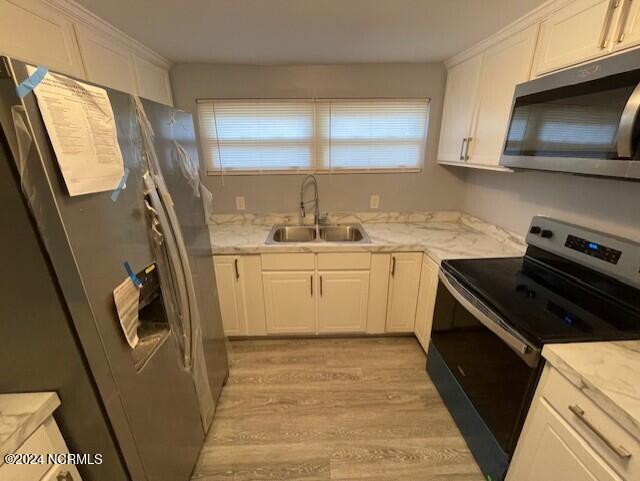 kitchen with light stone countertops, sink, stainless steel appliances, white cabinets, and light hardwood / wood-style flooring