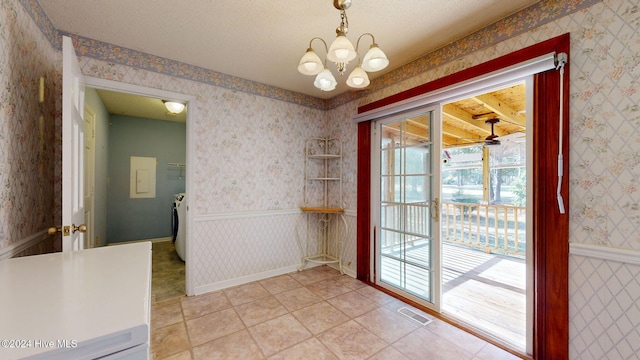 unfurnished dining area with tile patterned flooring, washing machine and dryer, a textured ceiling, and an inviting chandelier