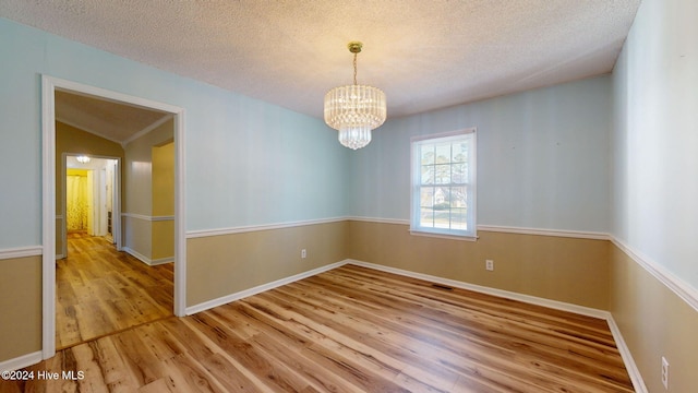 spare room featuring light hardwood / wood-style floors, a textured ceiling, vaulted ceiling, and a notable chandelier