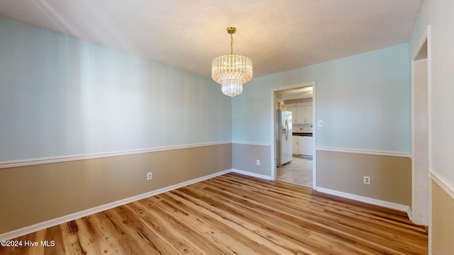 empty room featuring a textured ceiling, an inviting chandelier, and light hardwood / wood-style flooring