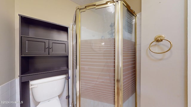 bathroom featuring tile walls, toilet, and a shower with door