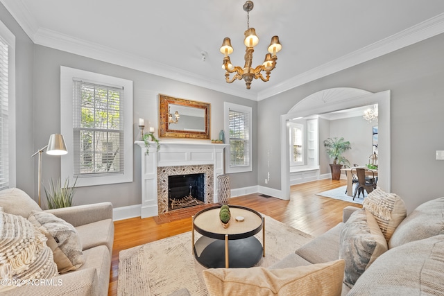 living room with light hardwood / wood-style floors, an inviting chandelier, crown molding, and a premium fireplace