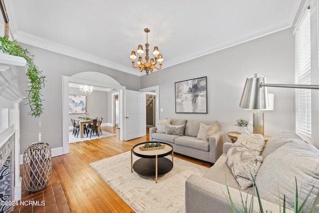 living room featuring hardwood / wood-style floors, ornamental molding, a brick fireplace, and an inviting chandelier