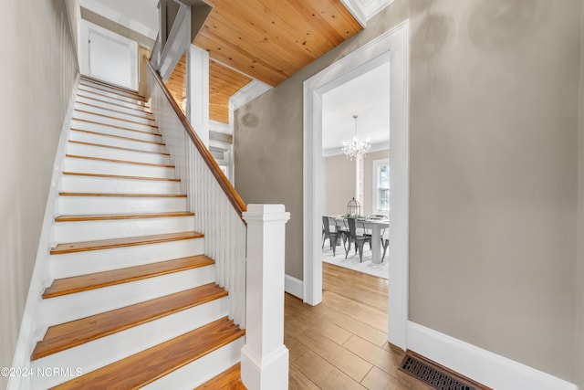 stairs featuring hardwood / wood-style floors, an inviting chandelier, and wood ceiling