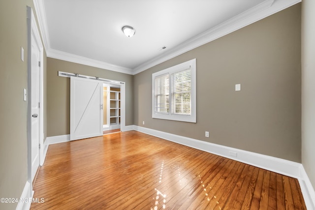 empty room featuring a barn door, crown molding, and light hardwood / wood-style floors