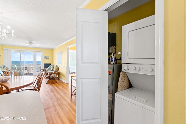 laundry area with ceiling fan with notable chandelier, stacked washer / drying machine, crown molding, and light hardwood / wood-style floors