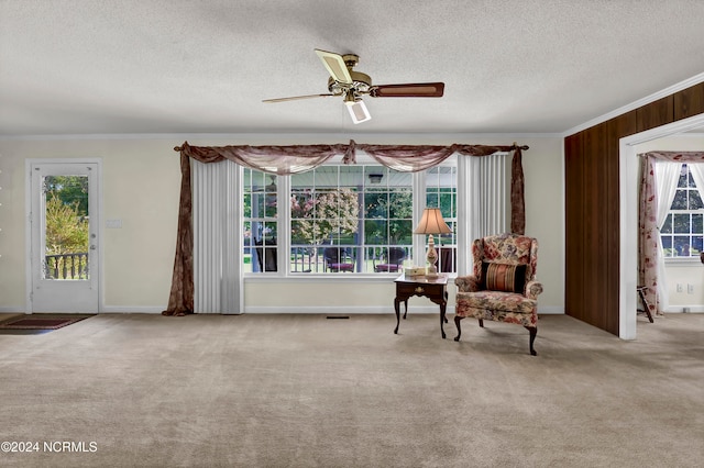 living area featuring wooden walls, crown molding, light colored carpet, a textured ceiling, and ceiling fan