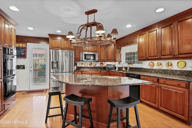 kitchen featuring a kitchen island, light wood-type flooring, black appliances, pendant lighting, and a notable chandelier