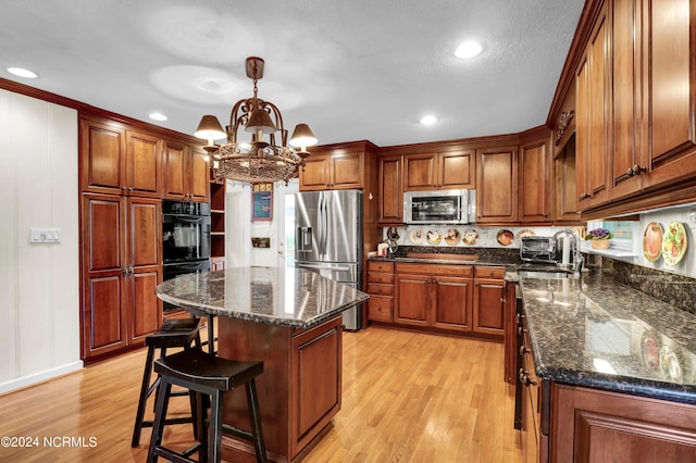 kitchen with a center island, stainless steel appliances, decorative light fixtures, a notable chandelier, and light hardwood / wood-style flooring