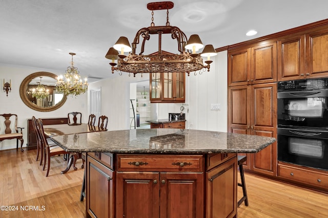 kitchen featuring a kitchen island, a breakfast bar area, hanging light fixtures, black double oven, and light hardwood / wood-style floors